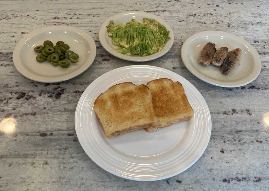 ingredients to make avocado toast: avocado, sardines, olives and toast